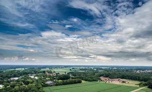 在德国的一条道路上，从空中俯瞰一个村庄边缘的一片耕地，那里有相连的森林区和树木，戏剧性的天空