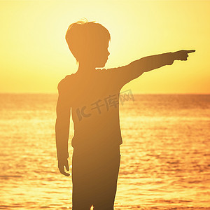 一个男孩的轮廓在日出日落时竖起大拇指在海洋的海边橙色天空橙色海洋男孩向侧面展示他的食指