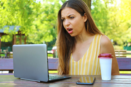 肆虐摄影照片_失望的女商人坐在公园里，看着笔记本电脑在一上午的辛勤工作后肆虐。