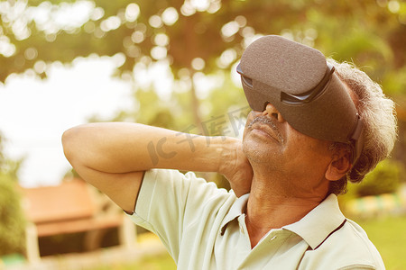 老年人使用 VR 谷歌眼镜进行锻炼，户外-老年人使用新技术的健身概念-老年人通过观看虚拟现实护目镜伸展双手。