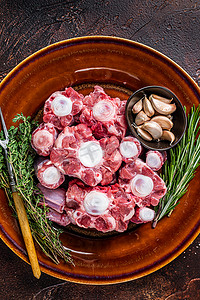 新鲜的未煮过的牛尾牛肉用香草在质朴的盘子上切肉。