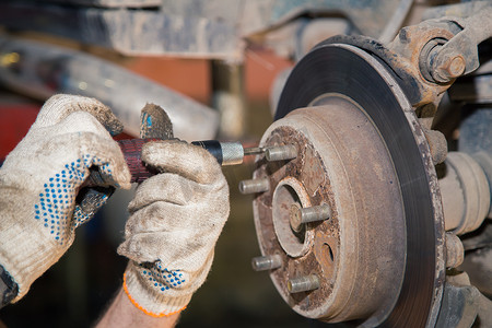 汽车轮毂维修摄影照片_手松开磨损生锈的后制动盘的螺栓。