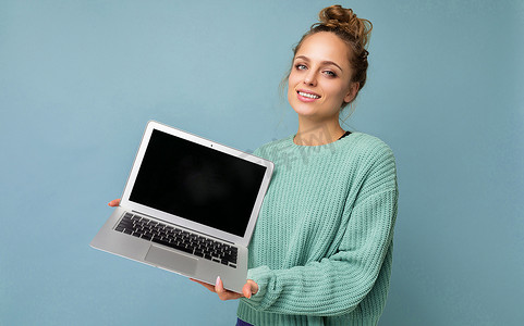 特写肖像照片的美丽 amiling 深色金发年轻女子聚集卷曲的头发看着相机拿着电脑笔记本电脑与空监控屏幕与模拟和复制空间穿着蓝色 longsleeve 隔离在浅蓝色墙壁背景