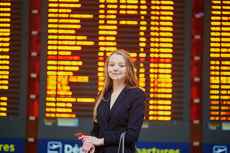 手提行李摄影照片_国际机场航站楼提着手提行李的女人，看着信息板