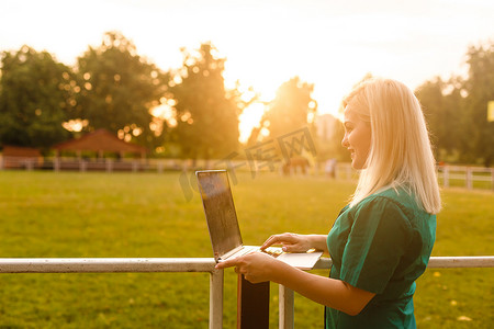 温暖的夏日，在公园里拿着笔记本电脑的金发美女