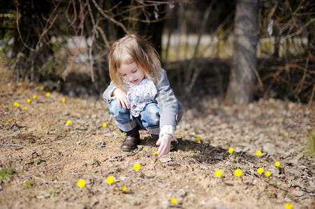 可爱的小花朵摄影照片_触摸春天花朵的小蹒跚学步的女孩