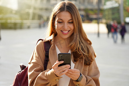 年轻开朗时尚的女人在城市街道上使用手机和短信。