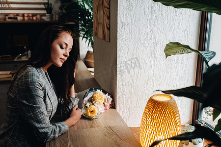 咖啡馆里一位留着长发的年轻欧洲女孩的画像，窗边放着一束花，一位身穿长发夹克的高个子女孩在咖啡馆里等着