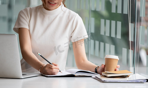 在家里用笔记本电脑在记事本中工作或在线学习的女性写作制作列表记笔记的裁剪照片手
