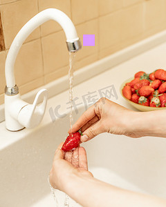 妇女们的手在厨房水槽的水流下清洗草莓和蓝莓。