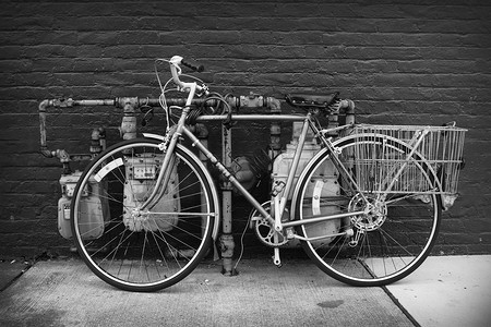 一辆自行车的黑白轮廓照片，后面有一个篮子，绑在公共管道上，比如自行车架