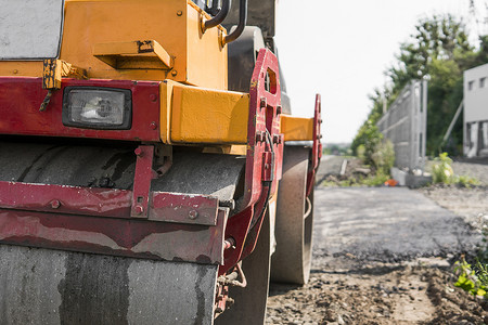橙色振动压路机站在沥青路附近的地面上进行道路施工和修复沥青路面工程与蓝天。