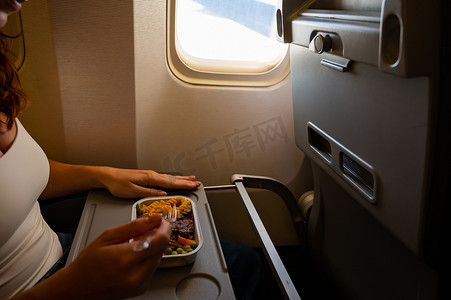 乘坐经济舱的白人女性在飞机上的小桌上吃午餐。