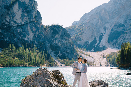 白云站摄影照片_新娘和新郎站在石头上俯瞰意大利的 Lago di Braies。