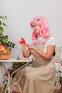 粉色假发摄影照片_戴着粉色假发的年轻女孩正在制作折纸
