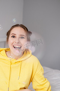 黄色迷人的年轻女子的画像，在明亮的灰色背景上的肥皂泡泡中。