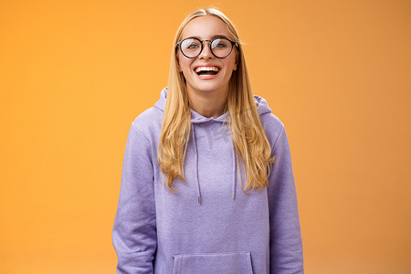 有魅力的快乐迷人的微笑女大学直学生戴着眼镜紫色舒适连帽衫笑着开心地笑着高兴地邀请同学站在橙色背景