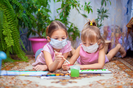 两个戴着防护口罩的女孩在家里或幼儿园的地板上涂上油漆