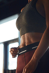 在健身房锻炼时穿着运动服的运动健身女性的垂直照片显示出完美的腹肌