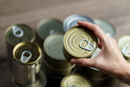 保守摄影照片_女人手拿着一组铝罐头食品。