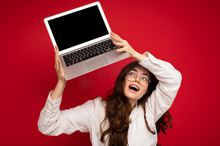 惊讶喜出望外美丽微笑快乐的年轻女子拿着电脑笔记本电脑看着上网本张开嘴穿着休闲智能衣服隔离在墙壁背景