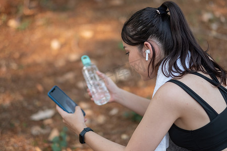 疲惫的健身女性在艰苦的训练后汗流浃背，在手机上听音乐休息