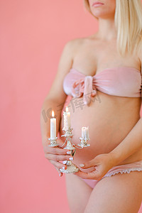 年轻快乐的孕妇穿着内衣，抱着肚子，点着蜡烛。