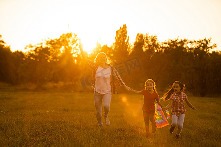 夏天，幸福的家庭母亲和孩子们带着风筝在草地上奔跑