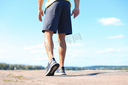 公路奔跑摄影照片_跑步者的脚在路上奔跑，特写在鞋子上，在日落或日出时在户外