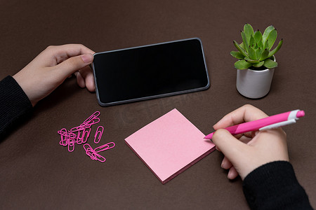 女人手拿着空白笔记，在手机旁边写新的消息更新想法。