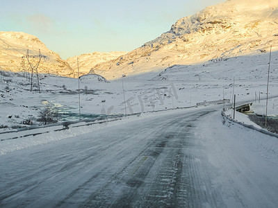 天气下雪摄影照片_日出时开车穿过挪威结冰的道路上的山脉。