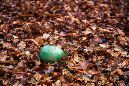 空的、干燥的玻璃罐掉进森林里的干树叶里，pollu