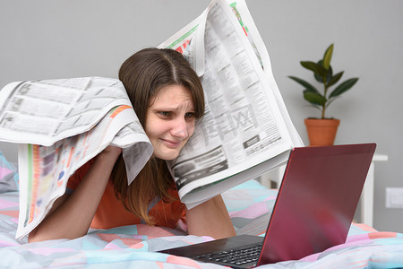 报纸女孩摄影照片_女孩把报纸放在头上，看着笔记本电脑屏幕试图找工作