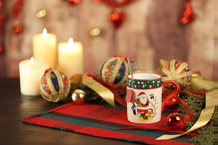 圣诞桌布上有空茶标签的圣诞杯，周围有松树枝、剪纸小饰品、点燃的蜡烛和悬挂在木制背景上的圣诞装饰，具有散景效果