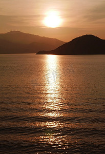 日落时的太阳、山脉、海洋和水波