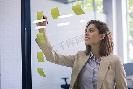 小麻薯贴纸摄影照片_有魅力的女商人在办公室的玻璃上贴上贴纸，并在上面写字。