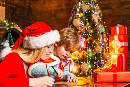 给孩子一封信摄影照片_妈妈和孩子给圣诞老人写一封信，上面写着圣诞礼物的愿望清单。圣诞室内。