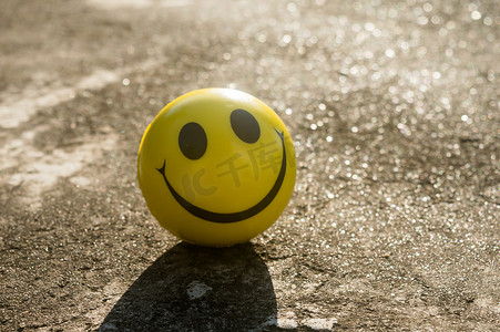 标志性的黄色笑脸，完美的圆圈，两只椭圆形的眼睛和一张半圆形的大嘴巴，代表着幸福的象征，与沙子和阴影背景隔绝。