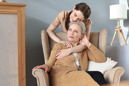 快乐的女儿拥抱年长的母亲，站在客厅的椅子后面，在家里享受温柔的时刻