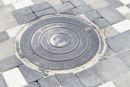 灰色水摄影照片_人行道上的新塑料井盖铺有灰色铺路板。