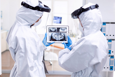 流行光摄影照片_穿着防护服的压力大的医生正在看数字牙科 X 光片