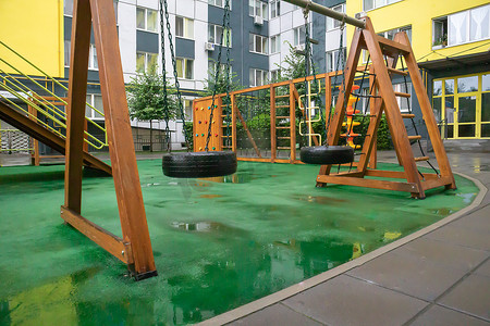 在一个雨天无人的夏日，一栋高层建筑的庭院里有一个由木材和塑料制成的现代化大型游乐场。