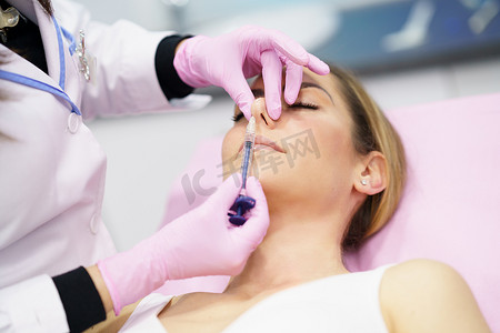 隆鼻手术摄影照片_医生通过在病人的鼻子里注射透明质酸来进行隆鼻手术。