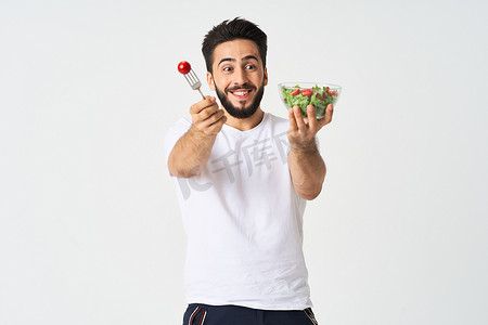 穿着t恤的人摄影照片_穿着白色T恤的快乐男人一盘沙拉蔬菜饮食