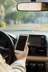 手握手机方向盘摄影照片_年轻的女司机在车里使用触摸屏智能手机和手握方向盘。