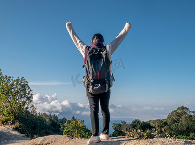暑假期间，年轻女旅行者举起双臂在山顶展示成功。