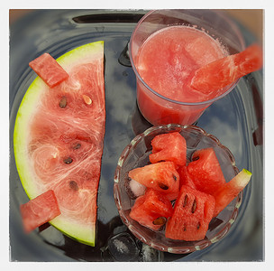好吃夏季摄影照片_冷却西瓜汁，切块和冰块，玻璃碗中的碎片和黑盘中的西瓜片，适合夏季和健康水果，也可保持身体水分饮料