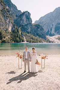 新娘和新郎在意大利 Lago di Braies 的背景下，以秋天的花柱拱门为仪式站好。