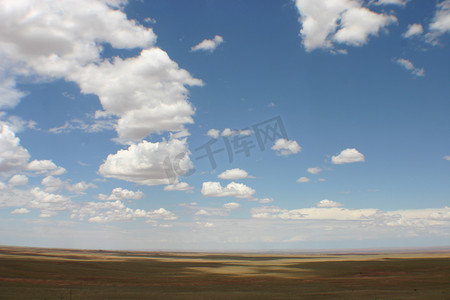新墨西哥州蓝色天空的全景照片，在平坦的沙漠地面上散落着云彩