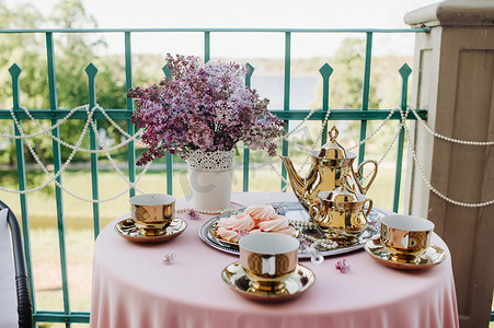 精致的早茶桌布置，桌上放着淡紫色的花、古董勺子和盘子，桌上铺着粉色桌布
